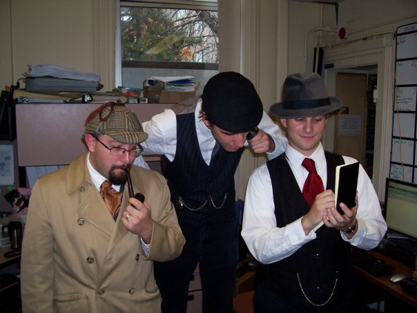 One person dressed as Sherlock Holmes and two dressed as Watson look at a notebook